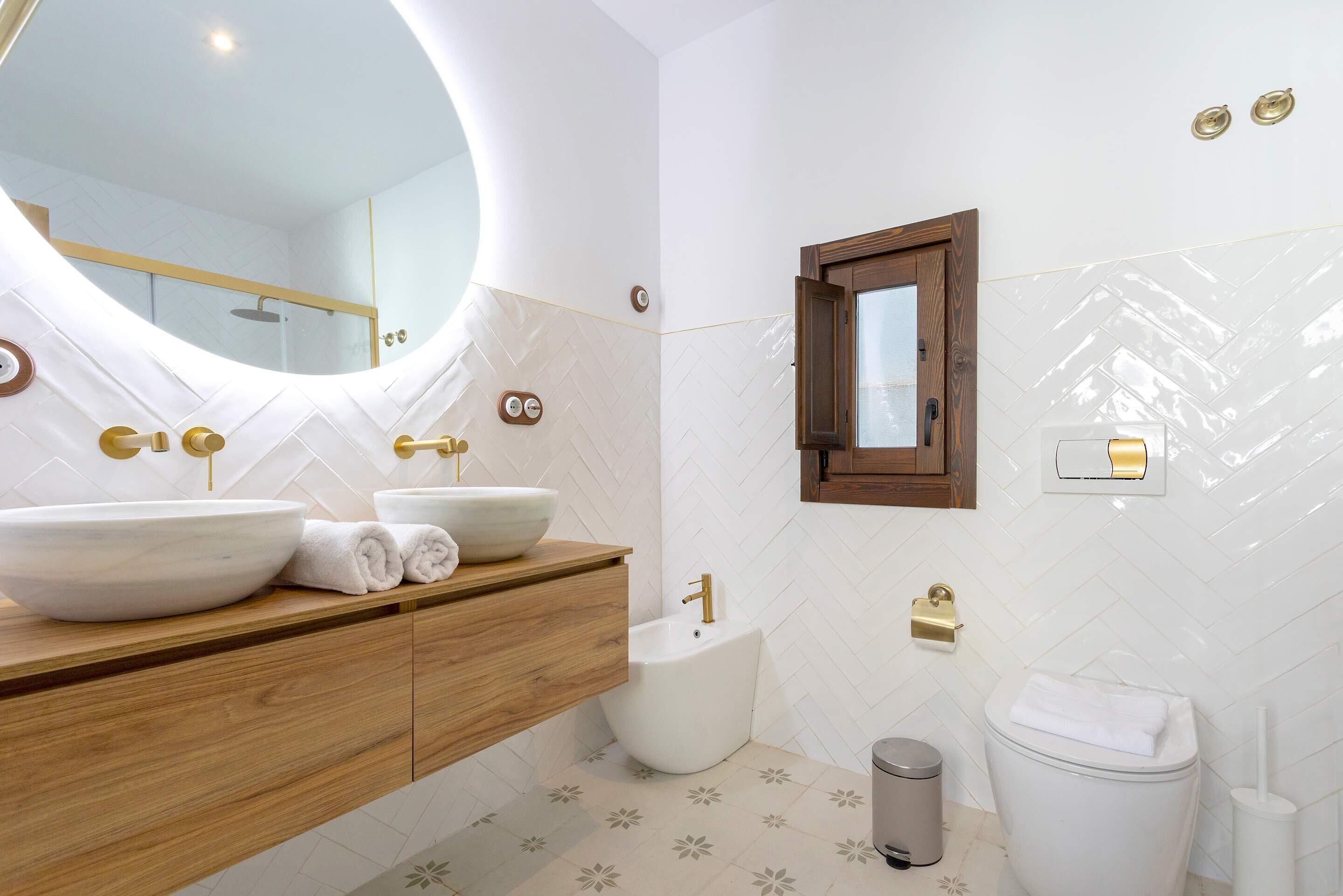 A modern bathroom with a large oval mirror, a wooden vanity, a bidet, and a toilet.