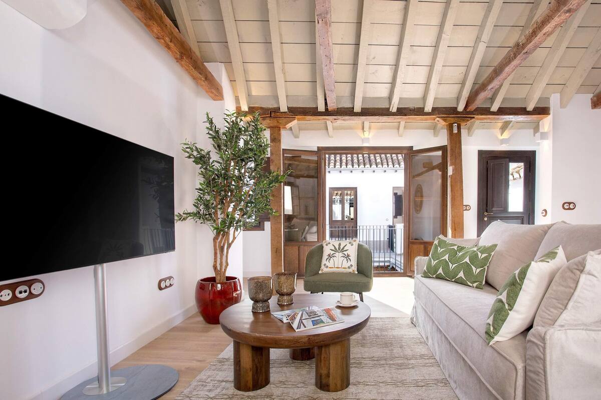 Ein Wohnzimmer mit Flachbildfernseher, rundem Couchtisch, Sofa, Sessel und einer Topfpflanze.