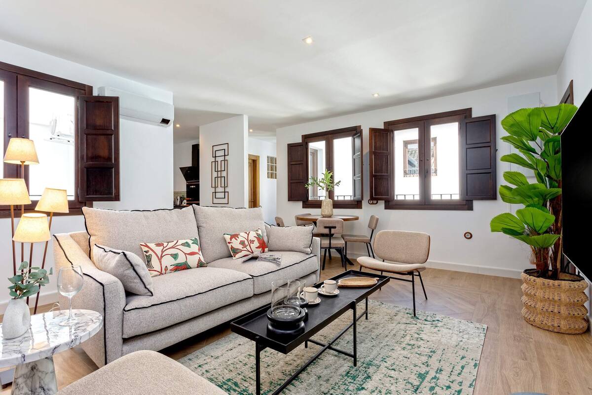 Ein Wohnzimmer mit einer Couch, einem Couchtisch und Sesseln. Im Hintergrund steht ein Esstisch.