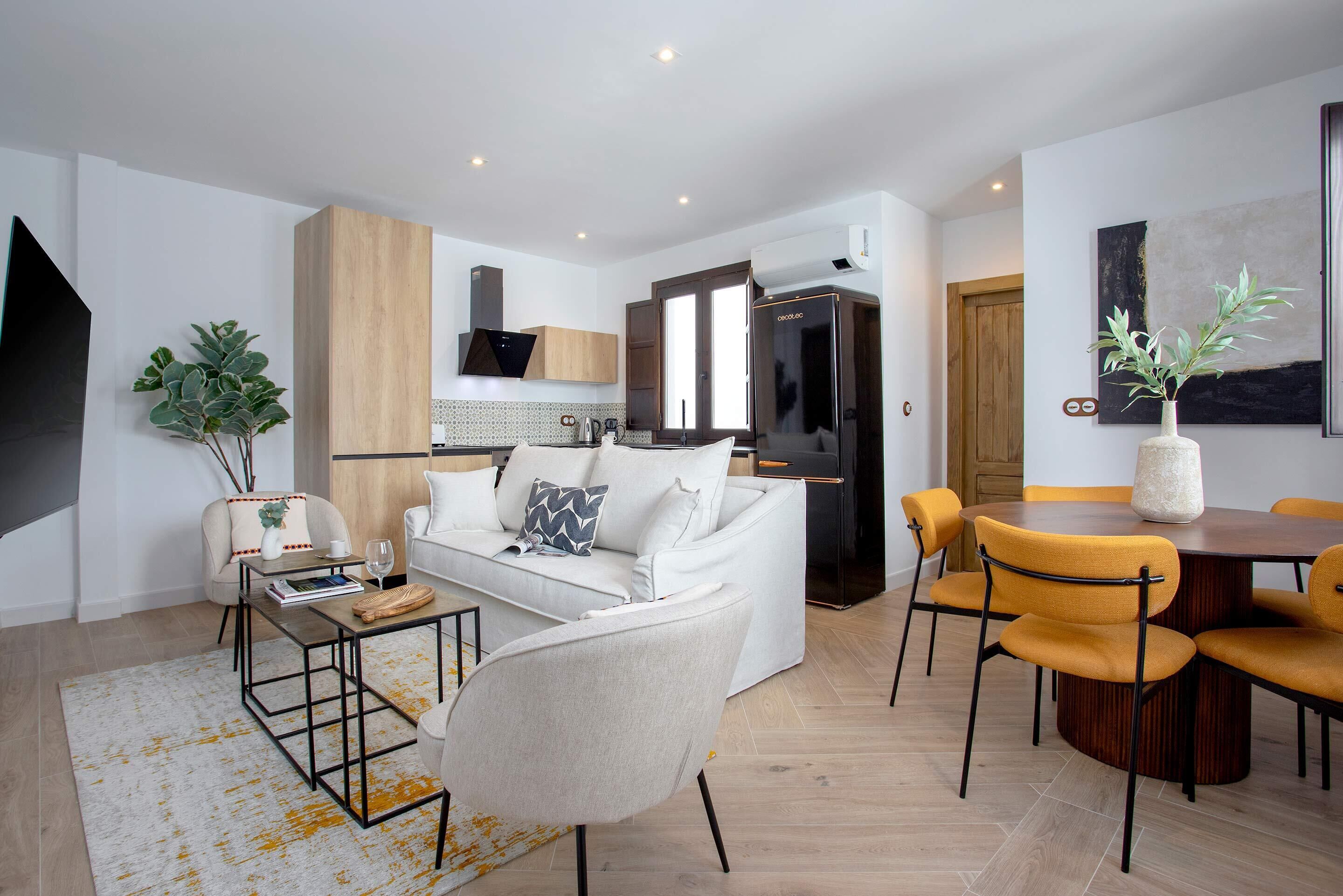 Un salon moderne avec un canapé blanc, une table basse et un coin repas avec des chaises jaunes.