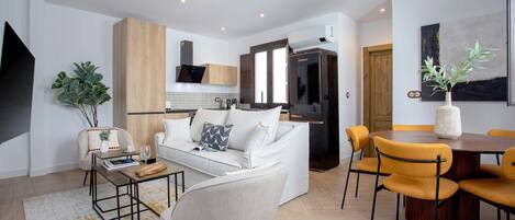 A modern living room with a white sofa, a coffee table, and a dining area with yellow chairs.