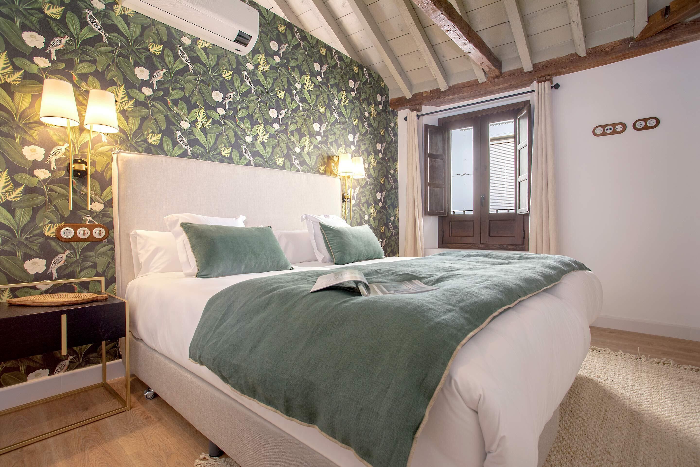A bedroom with a bed, bedside lamps, a nightstand, and a window with curtains.