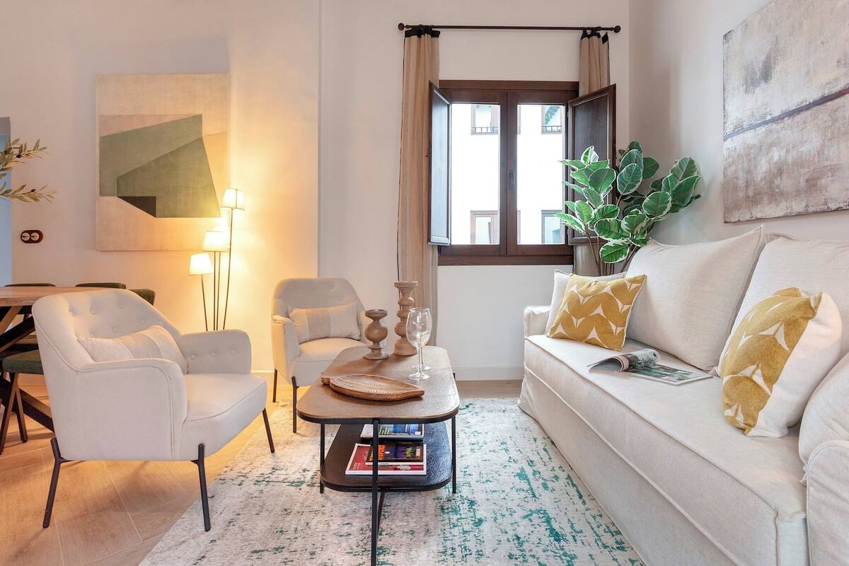 Ein modernes Wohnzimmer mit einer Couch, Sesseln, einem Couchtisch und einem großen Fenster mit Vorhängen.