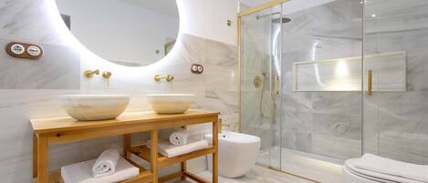 A modern bathroom with a round mirror, two sinks, a wooden vanity, a glass shower enclosure, and a toilet.