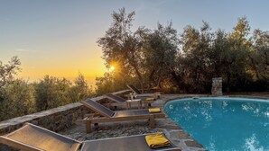 A poolside area with lounge chairs and a stone wall. - Castellare in Poggio 10 Emma Villas (Castellina in Chianti)