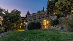 A stone building with a large arched window and a well-lit interior. - Castellare in Poggio 10 Emma Villas (Castellina in Chianti)