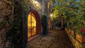 A stone building with an arched entrance, a wooden table and chairs outside, and a stone wall with a metal gate. - Castellare in Poggio 10 Emma Villas (Castellina in Chianti)