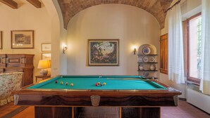 A pool table in a room with a brick arch ceiling, a painting, and a window with curtains. - Il Cerreto 11 Emma Villas (Pontedera)