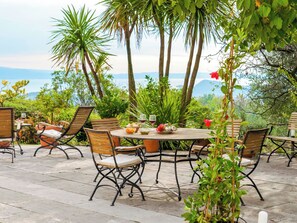 Patio esterno con tavoli e sedie rotonde, circondato da vegetazione rigogliosa e palme.
