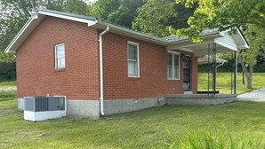 A red brick house with a covered porch, a small attached garage, and a well-maintained lawn. - Charming 2-bedroom cottage in Brodhead with WiFi and AC (Brodhead)