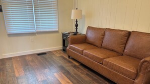 A room with a brown leather sofa, a lamp on a side table, and wooden flooring. - Charming 2-bedroom cottage in Brodhead with WiFi and AC (Brodhead)