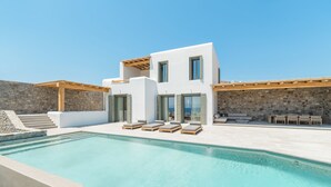 A modern house with a swimming pool, outdoor seating, and a stone wall.