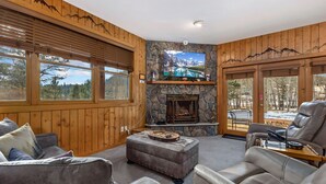 A cozy living room with a stone fireplace, leather sofas, and a large TV mounted above it. - Cozy Mountain Retreat • Near RMNP & Downtown (Estes Park)