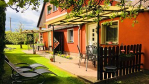 Una casa roja con jardín, mobiliario exterior y valla de madera.
