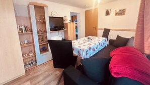 Un espacio habitable compacto con una mesa de comedor, un sofá, un televisor y una estantería.