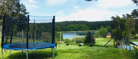 Un trampolín en un patio cubierto de césped, con un lago y un bosque al fondo.
