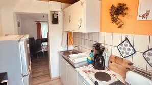 Una cocina compacta con techo de madera, armarios blancos, estufa y cafetera.