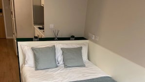 A bedroom with a bed, a bedside table, a mirror, and a small plant. - The Depot in Bath (Bath)