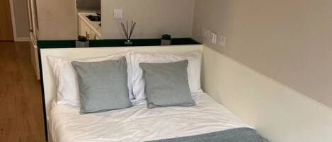 Un dormitorio con una cama, una mesita de noche, un espejo y una planta pequeña.
