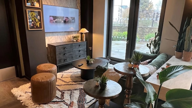 A modern living room with a sofa, two round tables, a TV, and various plants. - The Depot in Bath (Bath)