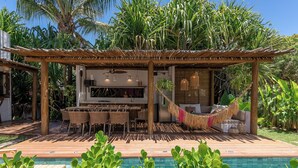 Een zwembadgedeelte met een houten pergola, zitplaatsen buiten en een hangmat.