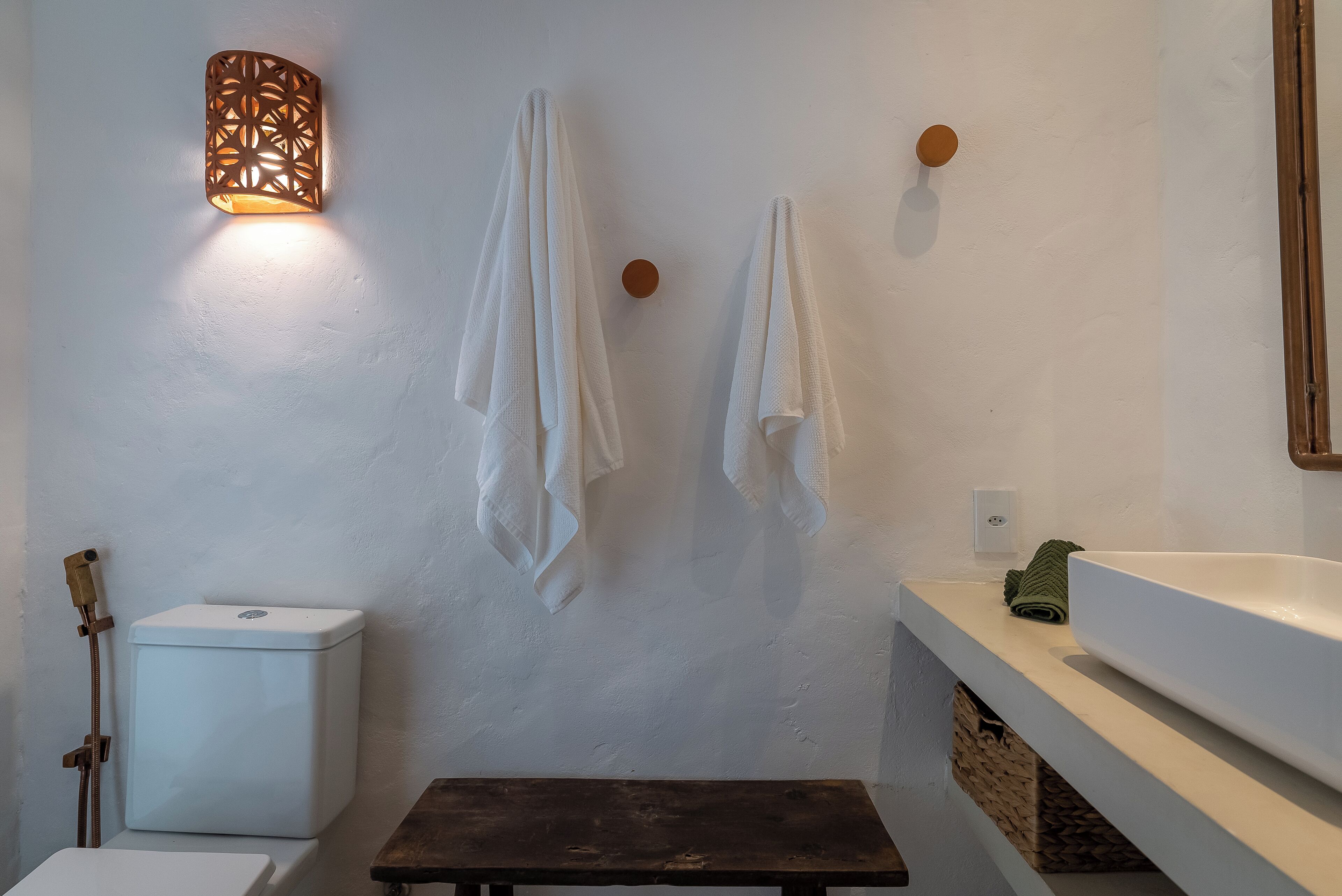A bathroom with a toilet, a sink, and a bench.