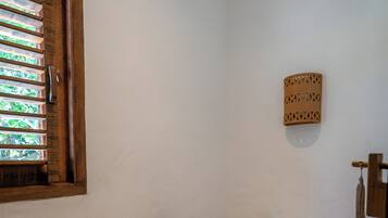 A small bathroom with a toilet, a wooden shelf, a wicker basket, and a window with blinds.