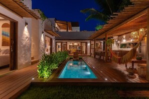 A pool area with a wooden deck, a small pool, and a seating area with a table and chairs. - Nossa Villa Caraiva (Porto Seguro)