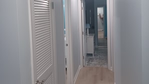 A hallway with white walls and a wooden floor, leading to a room with a blue wall and a mirror. - Modern 2BD/BA, 1.5 Blocks to Sea, Walk to Amenities w/ Pool, Linens & Parking (Virginia Beach)