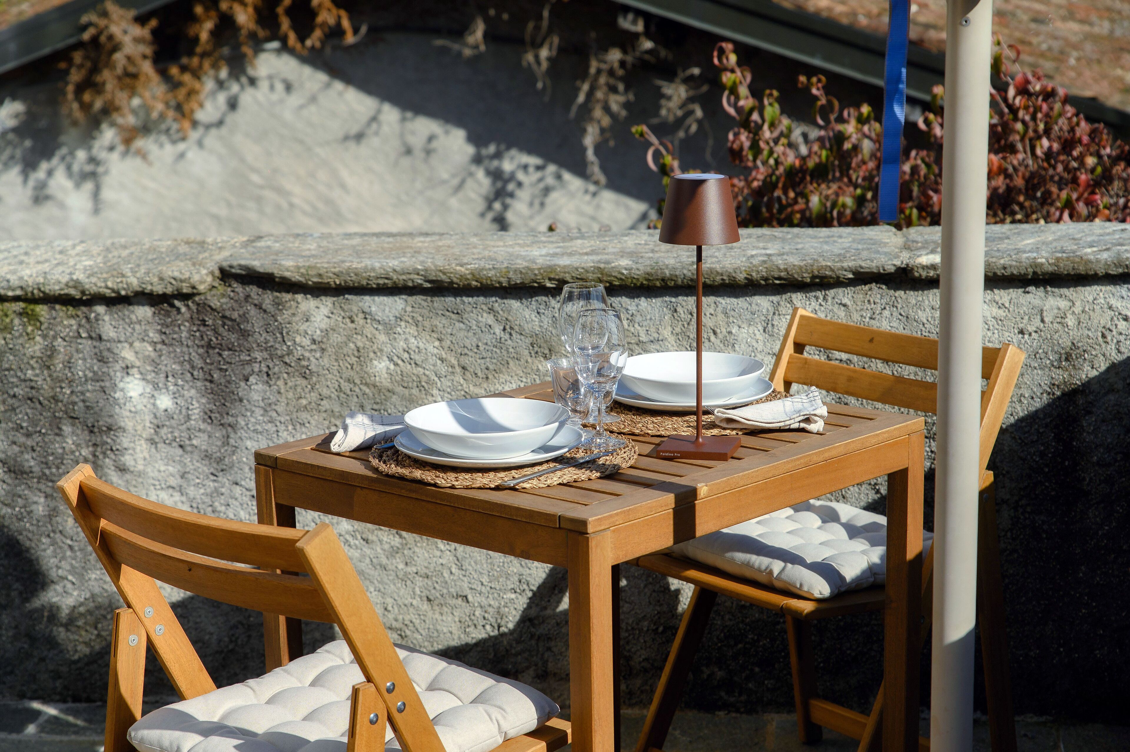 A wooden table with a placemat, two white plates, a wine glass, and a candle holder.