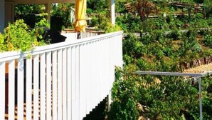 A covered balcony with a yellow umbrella, surrounded by lush greenery and a clear blue sky. - BLACK&WHITE vacation home (Niederösterreich)