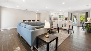 Een moderne woonkamer met een bank, salontafel en stoelen. In de achtergrond is een keuken zichtbaar met een eethoek.
