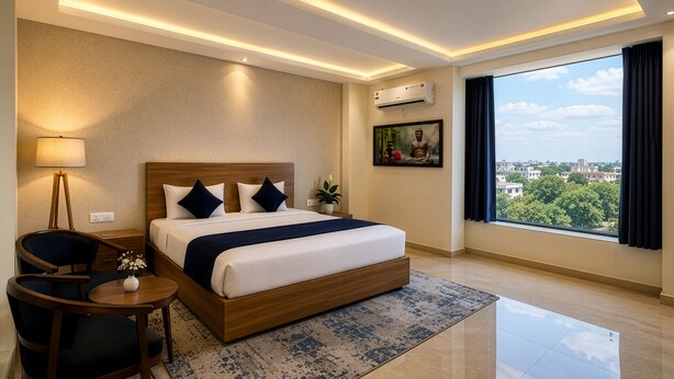 A modern hotel room with a large bed, a desk, a chair, a potted plant, an air conditioner, and a city view.