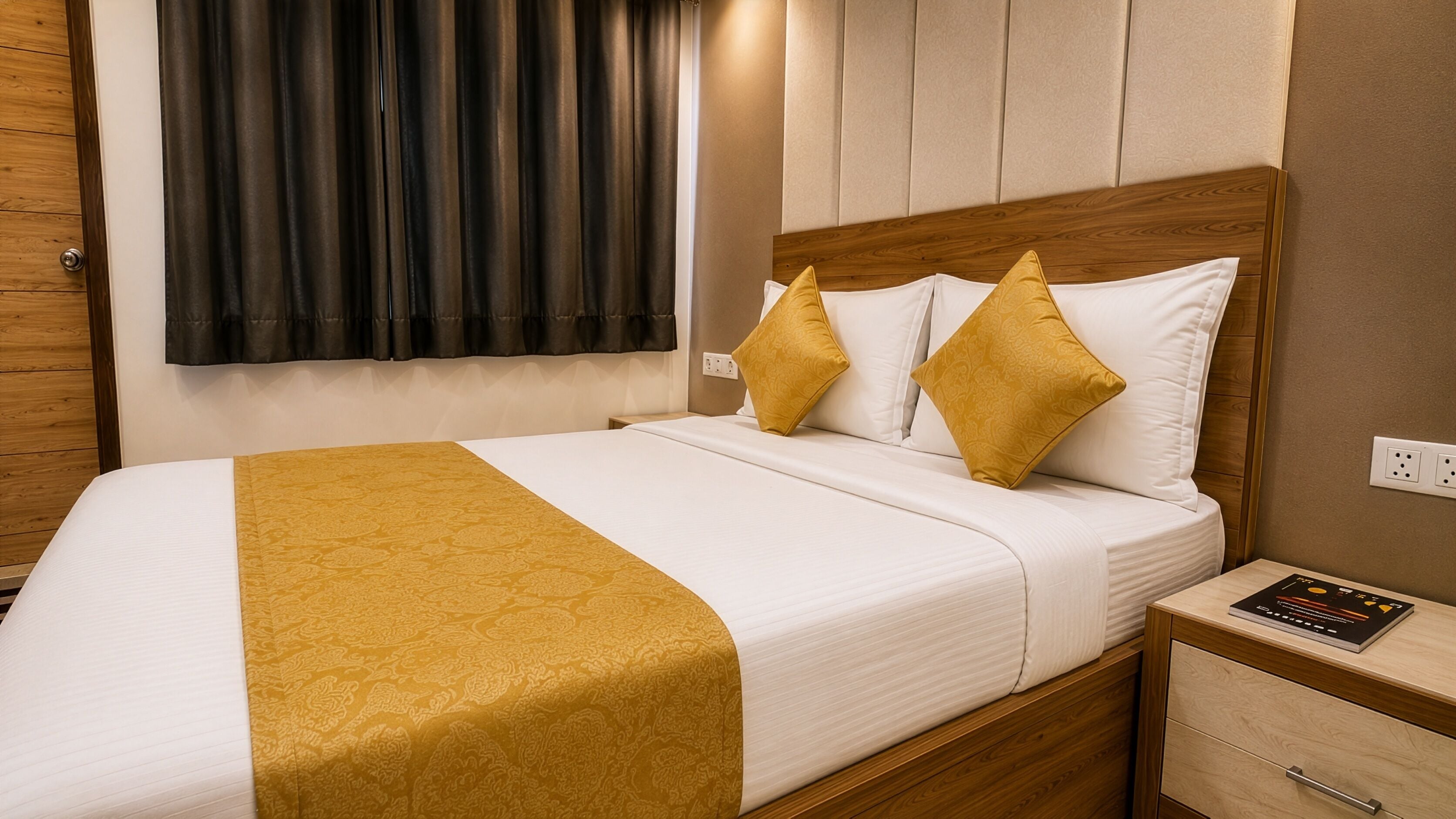 A neatly made bed with a white and gold bedspread, two gold pillows, and a wooden headboard.