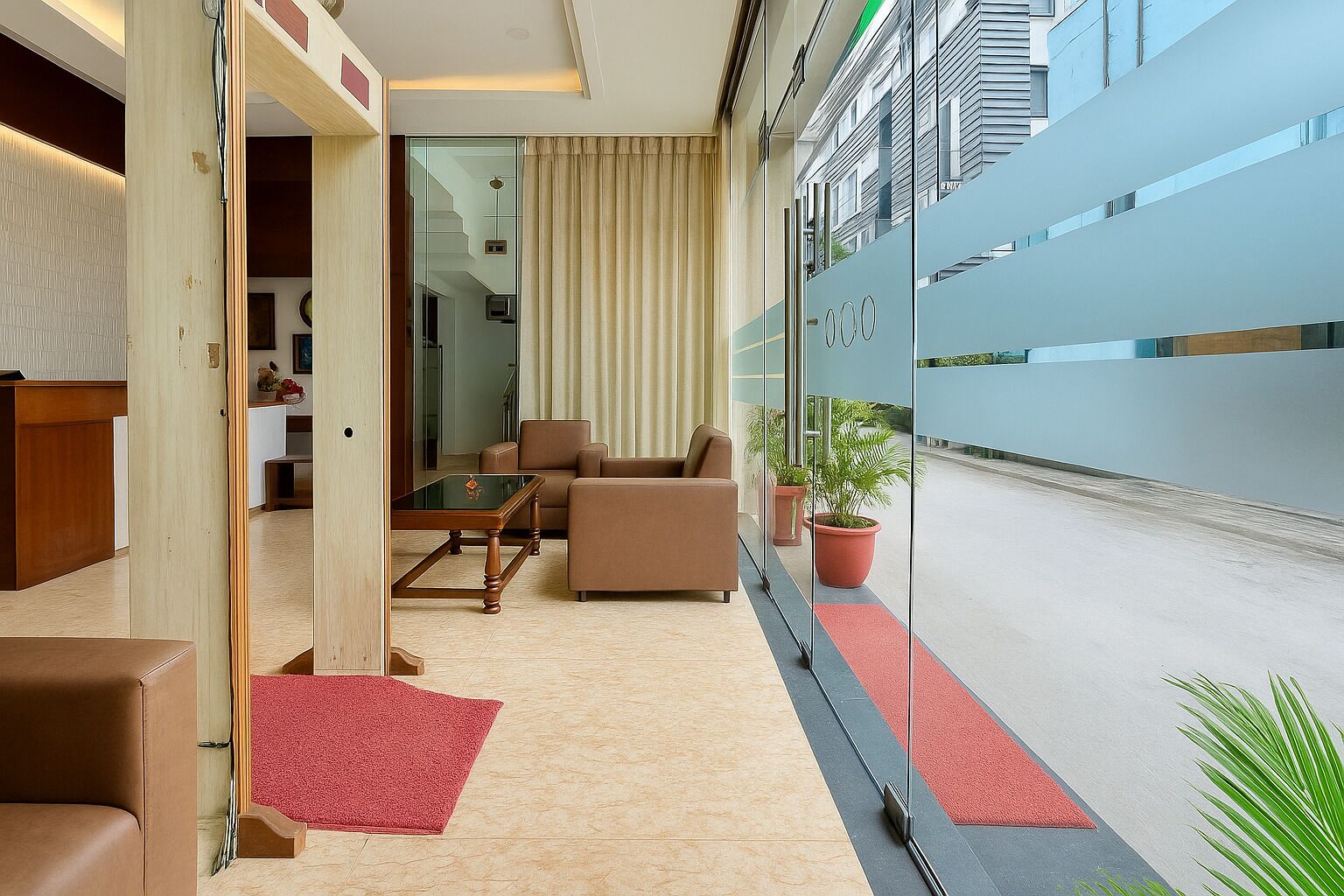 En moderne hotellobby med et siddeområde, en glasvæg med udsigt over byen og en rød løber til indgangen.