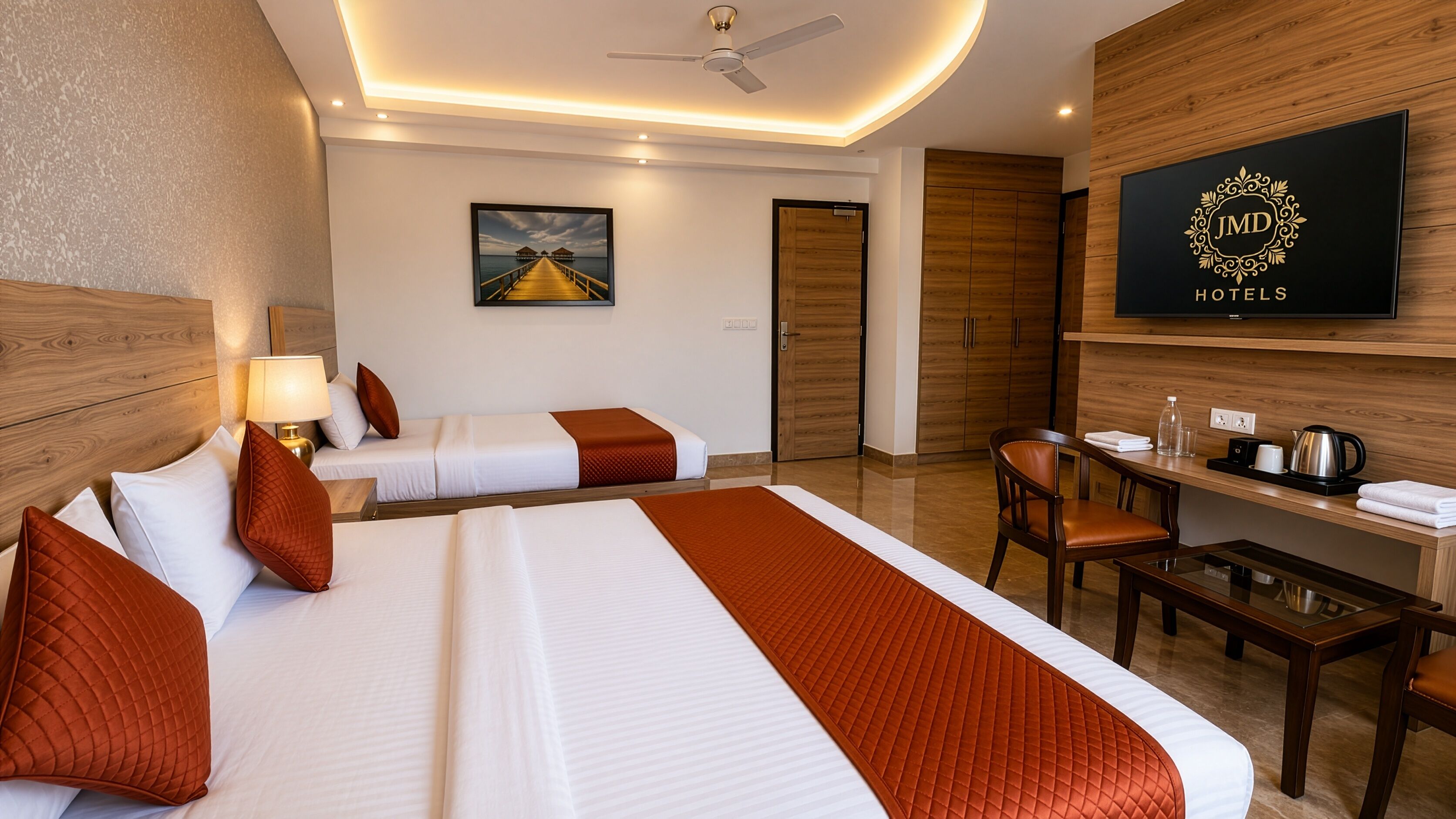 A hotel room with two beds, a desk, a chair, a television, and a ceiling fan.