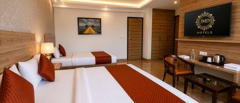 A hotel room with two beds, a desk, a chair, a television, and a ceiling fan.