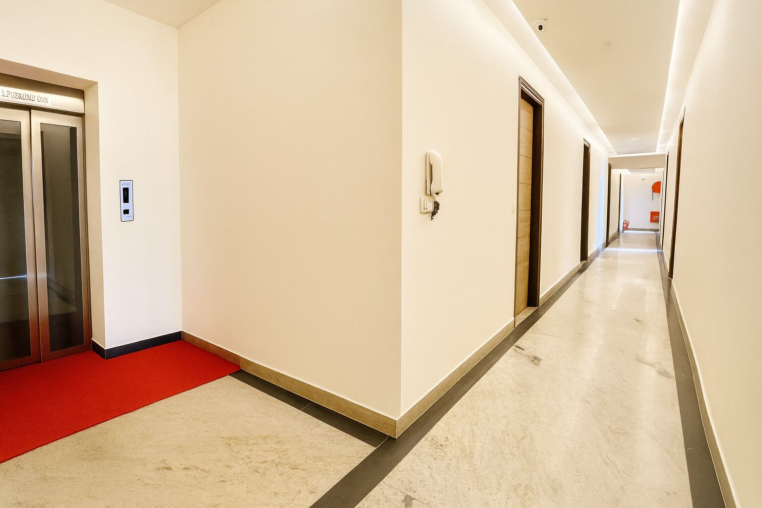 A hotel corridor with elevators, a red carpet, and a long hallway.