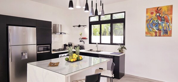 A modern kitchen with a central island, stainless steel appliances, and a large window providing natural light.