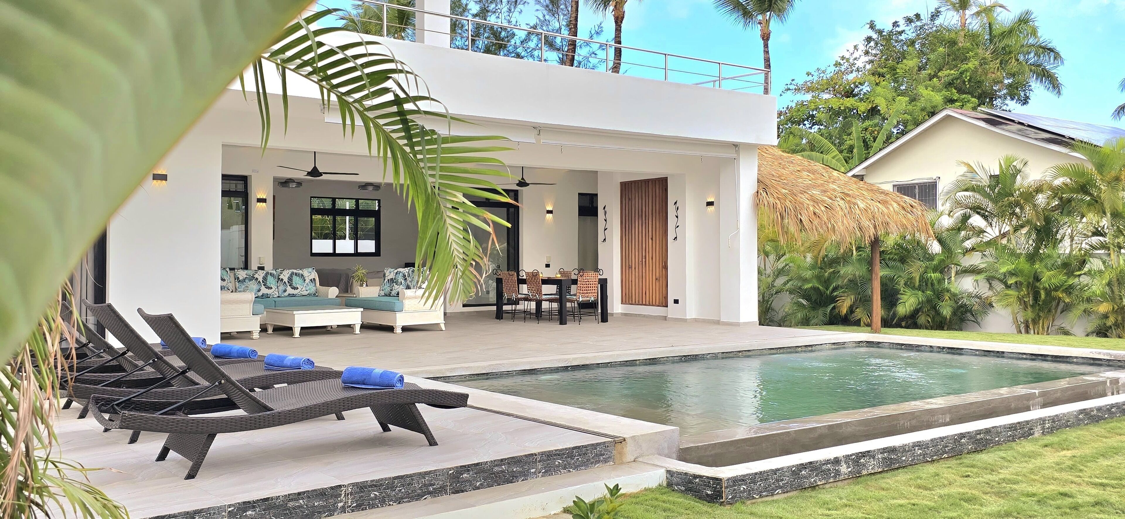 A modern house with a pool, lounge chairs, and a dining area.