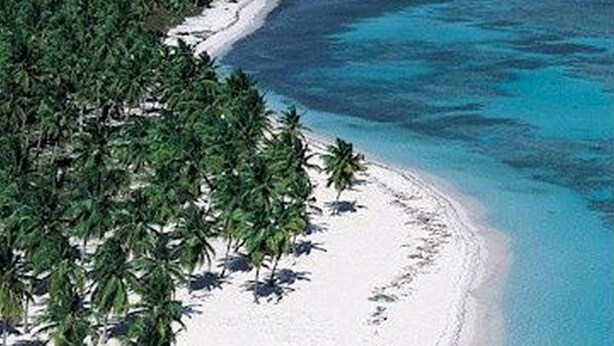 Vue aérienne d’une île tropicale avec son sable blanc, ses eaux turquoise et limpides, et ses nombreux palmiers.