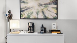 Een wit bureau met een lamp, een koffiezetapparaat, een speaker en een bordje met de tekst 'WLAN'.