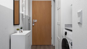 Een wasserette met een houten deur, een wasmachine en een klein plantje op een aanrecht.