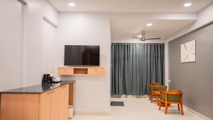 A modern living room with a flat-screen TV mounted on the wall, wooden cabinets, a dining area with two chairs, and a ceiling fan. - Silver waves Beach Stay (Udupi)