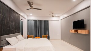 A modern bedroom with a bed, bedside tables, a TV, and a ceiling fan. - Silver waves Beach Stay (Udupi)