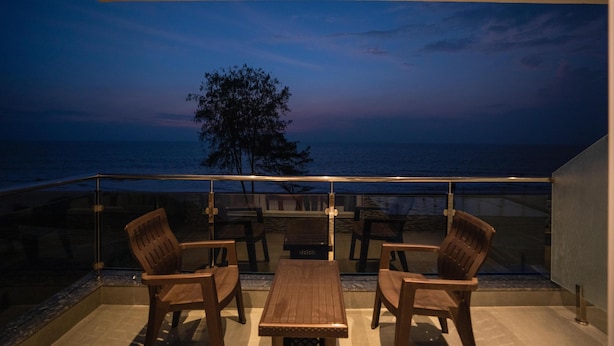 A balcony with a view of the ocean at dusk, featuring wooden furniture and a glass railing. - Silver waves Beach Stay (Udupi)