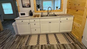 A compact kitchen with white cabinets, a wooden countertop, a sink, a microwave, and a mirror above the sink.