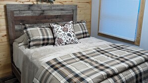 A wooden-paneled bedroom with a bed, a headboard, a window with blinds, and a wall-mounted wreath.