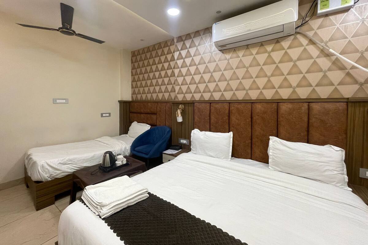 A hotel room with two beds, a ceiling fan, an air conditioning unit, and a geometric-patterned wall.