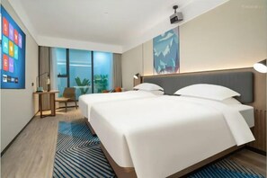 Une chambre d’hôtel avec un grand lit, un bureau, une chaise et une grande fenêtre donnant sur un paysage verdoyant.